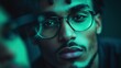 © Dulemegapixel - A young man in stylish glasses is captured in dramatic, teal lighting, exhibiting a sense of mystery and introspection, adding depth to the moody portrait.