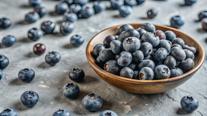 A wooden bowl filled with ripe blueberries sits amidst numerous scattered berries on a rustic grey surface, illuminated by soft, natural light, highlighting their freshness