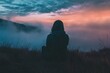 © atar - Silhouette of a woman sitting alone on a hilltop overlooking a misty valley at sunset