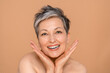 © InsideCreativeHouse - Closeup portrait of gorgeous happy middle aged mature woman senior older 50 year lady looking at camera touching her face isolated on beige background. Ads of lifting anti wrinkle skin care, spa.