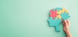 © netrun78 - A child's hand connects colorful puzzle pieces in a puzzle head shape on a pastel green background, symbolizing creativity, decoration, and minimalism in an engaging flat lay design