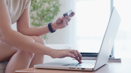 A woman is using a laptop computer to make a purchase. She is holding a credit card in one hand and a laptop in the other. Concept of convenience and modern technology