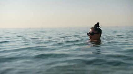 Sticker - A Woman Swimming Gracefully in the Serene and Calm Ocean Waters While Wearing Sunglasses