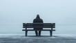 © Irina Kozel - A solitary figure in a hooded jacket sits on a bench by a foggy waterfront, evoking a sense of loneliness and introspection