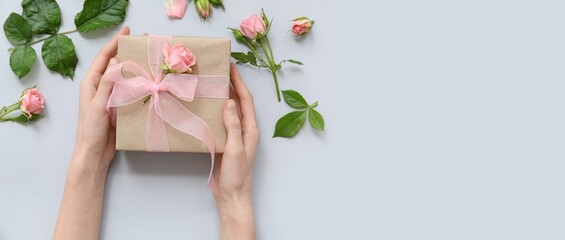 Wall Mural - Female hands, beautiful gift box and roses on light background with space for text, top view