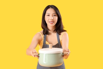 Wall Mural - Young beautiful Asian woman with saucepan on yellow background