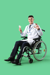 Wall Mural - Young male doctor in wheelchair with pills on green background