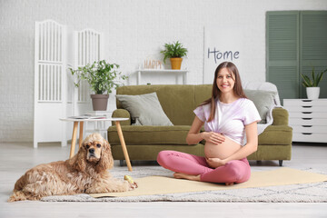 Poster - Beautiful sporty young pregnant woman with cocker spaniel practicing yoga at home