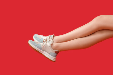 Legs of young woman in stylish sneakers on red background