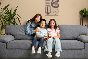 Sticker - Beautiful young happy Asian mother with her cute little children sitting on sofa at home