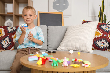 Wall Mural - Cute little boy on sofa sculpting from plasticine at home