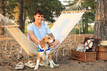 Wall Mural - Young man with cute Beagle dog sitting in hammock outdoors