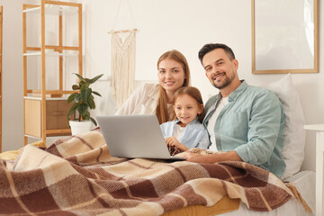 Canvas Print - Little girl and her parents with warm plaid using laptop in bedroom