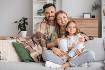 Canvas Print - Little girl and her parents with warm plaid sitting on sofa at home