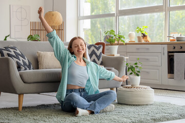 Poster - Happy young woman sitting on carpet in kitchen