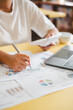 © Satori Studio - Close-up of a business professional analyzing financial data with charts and graphs on a desk, using a calculator and laptop.