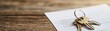 © Tonton1541 - A close-up of house keys resting on a wooden table next to a paper document, symbolizing home ownership and property management.