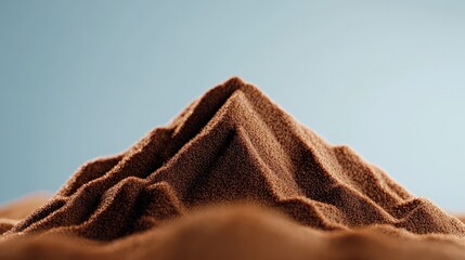 A close-up of a brown sand mountain, beautifully textured against a soft blue backdrop, ideal for artistic or nature-themed projects.