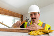 © Bogdan Pictures - A skilled construction worker expertly uses a hammer while donning a safety vest and helmet, completely focused on the important task of house remodeling and renovation activities within the interior