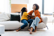 © Maria Vitkovska - Cute african american girl tickling her mother at sofa at home