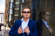 © Alex Vog - Portrait of strong man businessman in blue suit and glasses near building in business district, thoughtful looking at camera. Lovely male visit corporate company in financial area. Copy ad text space