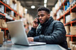 © eshana_blue - Warehouse worker is using a laptop and talking on a mobile phone, managing orders in a distribution center