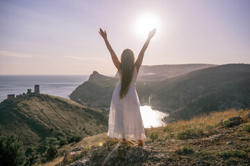 Wall Mural - A woman stands on a hill overlooking the ocean. She is wearing a white dress and has her hands on her head. The scene is serene and peaceful, with the woman looking out over the water.