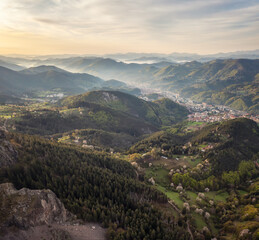 Wall Mural - A spring mountain valley at sunrise with rich vegetation and spruce dark dense forests and a small picturesque town of Smolyan nestled between the slopes, Rhodopi Mountains, Bulgaria.