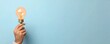© ParinApril - A hand holding a glowing light bulb against a pastel blue background, symbolizing creativity and innovative ideas.