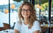 © Georgii - A candid photo of an attractive woman with glasses smiling at a cafe with a beautiful view of the outdoors