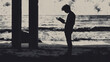 © Junya - silhouette of a person standing and reading book on the beach.