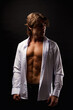 © Alex Vog - Sporty man in unbuttoned white shirt with abs muscle press posing in shadow at black, studio shot. Portrait of handsome guy with perfect muscular sexy torso, advertising model pose. Copy ad text space