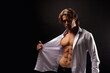 © Alex Vog - Perfect young man fashion model showing unbuttoned white shirt with abs muscle press poses in shadow at black. Portrait of stylish guy with perfect muscular sexy torso, studio shot. Copy ad text space