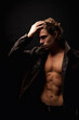 © Alex Vog - Handsome guy fashion model in unbuttoned image leather jacket with lovely muscular sexy torso, strong look. Perfect young man with abs muscle press posing in black studio shadow. Copy ad text space
