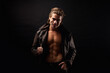 © Alex Vog - Handsome guy fashion model in unbuttoned leather jacket with abs muscle press posing in black studio shadow, strong look. Perfect young man with lovely muscular sexy torso, image. Copy ad text space