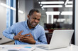 © Liubomir - Mature businessman visibly in discomfort holding chest, sitting at desk with laptop open. Office ambiance with modern lighting. Scene capturing moment of unexpected pain during work setting.