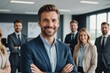 © ThomasLENNE - smiling confident business leader looking at camera and standing in an office at team meeting