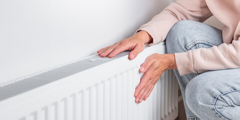 Woman warming hands near heating radiator at home, resource management during colder seasons