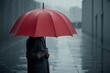 © astiva - A serene and moody scene depicting a solitary figure standing under a vibrant red umbrella on a rainy day, with droplets of water glistening on the fabric, capturing the tranquility of the moment.