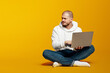 © Davidovici - Thoughtful young bearded man sitting on floor, holding laptop computer and looking away at empty space for text, isolated over yellow background