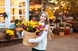 © stock_studio - Cute smiling teen girl in a sweater, skirt  posing with bouquet of autumn flowers in basket. Young fashionable girl in knitted clothes with chrysanthemum flowers on backyard at home.