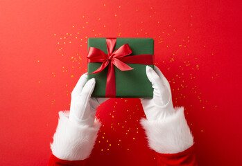 santa claus hands holding a beautifully wrapped green gift box with a red ribbon against a festive r
