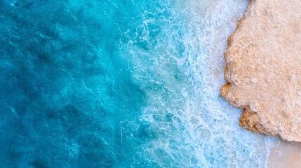 Wall Mural -  From above, a beach is depicted with crystal-clear blue water and a prominent rock outcropping in the foreground