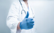 © Toowongsa - Close up medical worker hand in blue glove isolated on white background, medicine and treatment concept. Thumbs up sign.