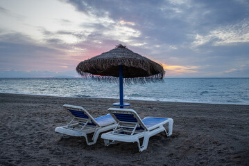 two couches and an umbrella on the beach. Spain