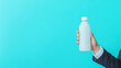 © Nakarin - A close up of hand in formal attire holding white water bottle against vibrant turquoise background, conveying sense of professionalism and refreshment