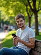 © Derek Brumby - A relaxed young man is casually sitting on a park bench, enjoying leisure time while engaging with his phone, surrounded by lush green scenery and tranquility.