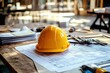 © Najikung - A yellow hard hat rests on architectural plans, symbolizing construction, safety, and design in a workspace.