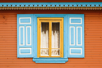 Wall Mural - Wooden rustic window in small cottage house. Vintage yellow paint wall. Transparent glass window with lace curtain. Blue color shutter. Decorative triangle shapes pattern.