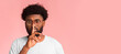 © Prostock-studio - Quiet african guy in glasses showing hush gesture over pink background, panorama with free space